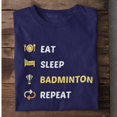 Folded navy blue T-shirt with Eat Sleep Badminton Repeat text and icons on wooden surface