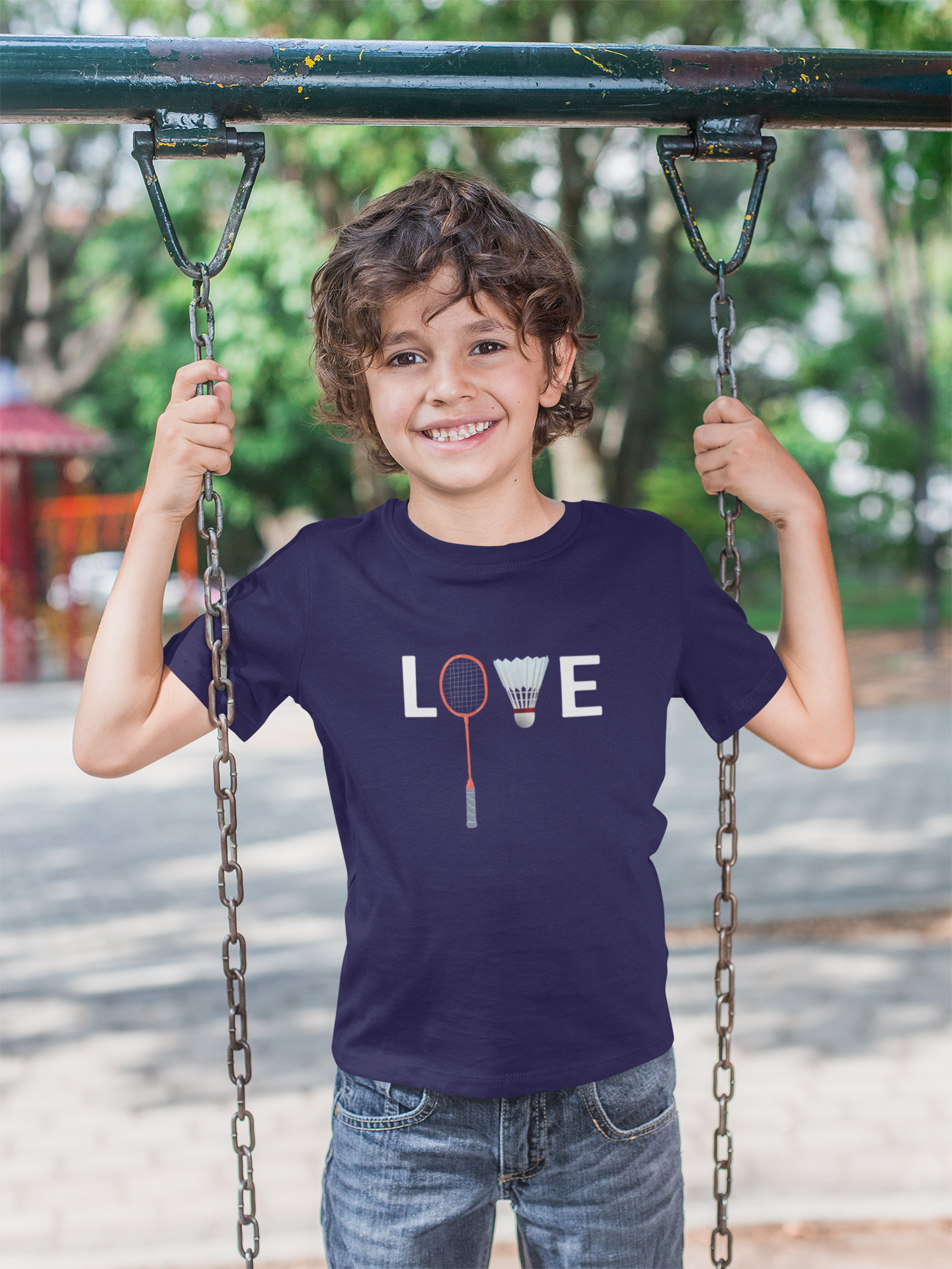 Smiling boy on swing wearing navy blue t-shirt with badminton love design outdoors