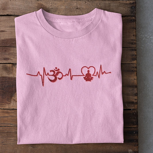 Folded pink t-shirt with red heartbeat, Om symbol, heart, and meditating figure graphic on wooden surface